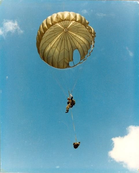 A Marine paratrooper descending under an open parachute against a blue sky